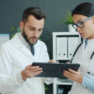 Two healthcare professionals, one male and one female, review information on a tablet in a modern office setting, indicating collaboration in patient care.