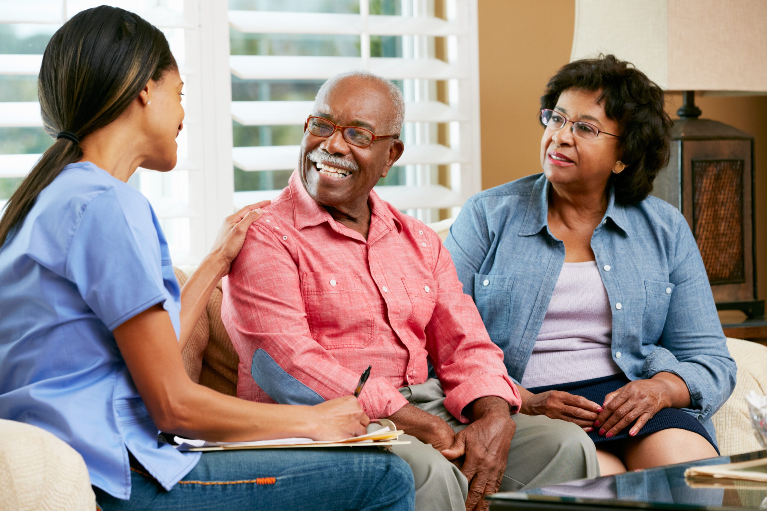 A healthcare professional converses with an elderly couple in a cozy living room, fostering a supportive dialogue about their care and well-being.