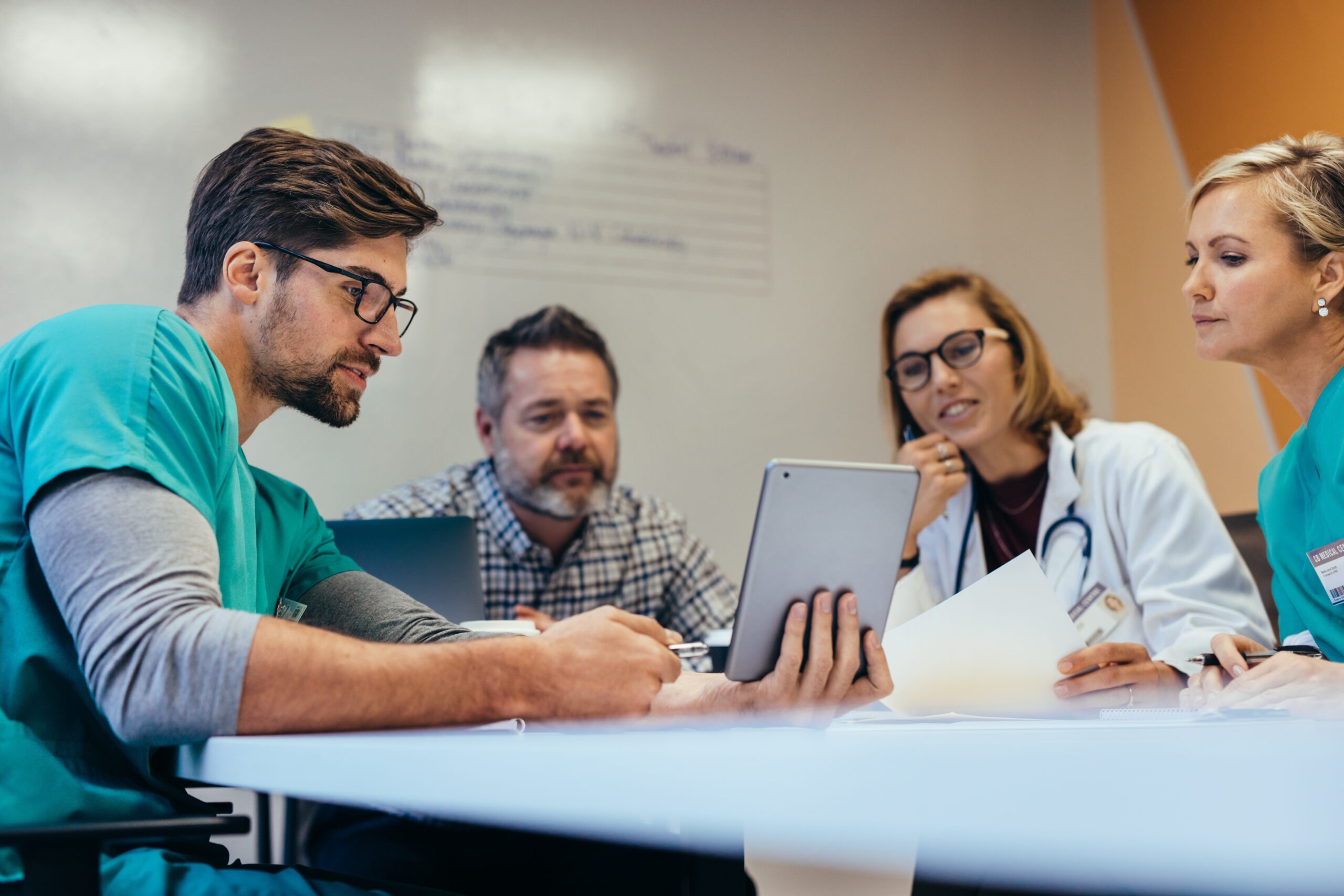 Medical professionals collaborate around a table, analyzing data on a tablet. The image emphasizes teamwork in healthcare decision-making.